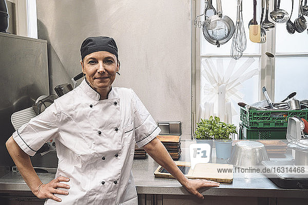 Portrait of confident mature chef with hand on hip in commercial kitchen