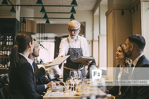 Kellner gibt Geschäftsleuten im Restaurant das Menü