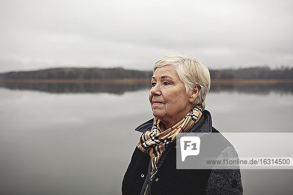 Lächelnde runzlige Frau schaut am See gegen den klaren Himmel weg