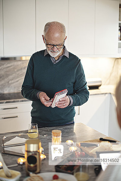 Älterer Mann nimmt Tabletten während er zu Hause an der Kücheninsel steht