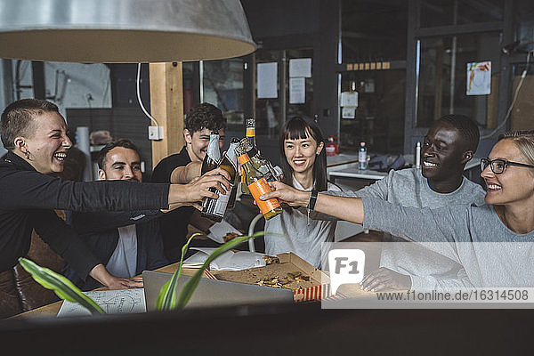 Lächelnde Mitarbeiter stoßen am Arbeitsplatz auf Bier an