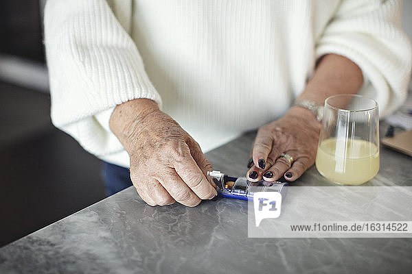 Midsection of senior woman taking pills at home