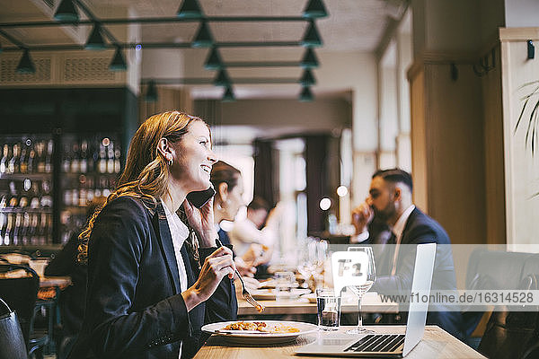 Lächelnde Geschäftsfrau beim Essen im Restaurant am Smartphone