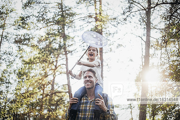 Lächelnder Vater trägt glückliche Tochter auf der Schulter beim Waldspaziergang