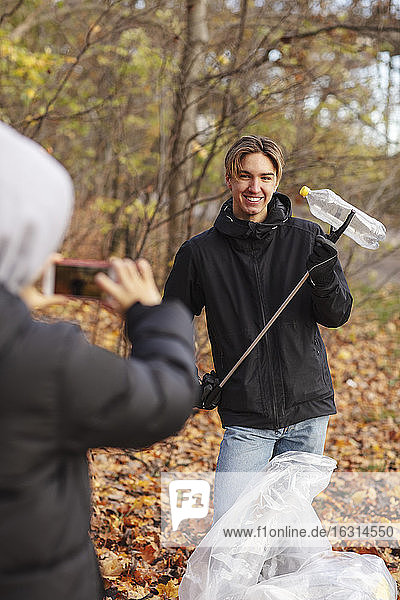 Teenager fotografiert im Herbst einen Freund mit einer Plastikflasche im Park