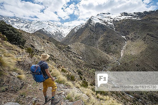 Hiker on a hiking trail  hiking trail Vereda de la Estrella  behind Sierra Nevada with summits Mulhacén and Pico Alcazaba  snow-covered mountains near Granada  Andalusia  Spain  Europe