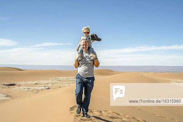 Vater geht mit huckepack 2 Jahre altem Sohn durch Sahara-Wüste in Marokko