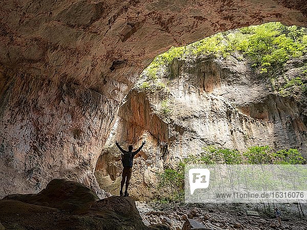 Wanderer streckt die Arme in die Luft  Höhle Cueva de La Ermita  Schlucht  steile Felswände der Garganta Verde  Sierra de Cádiz  Provinz Cádiz  Spanien  Europa