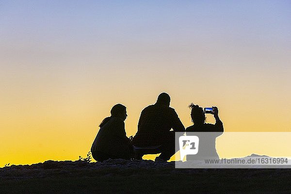 Young woman and men  twilight  talking  taking pictures with smartphone Baden-Württemberg  Germany  Europe