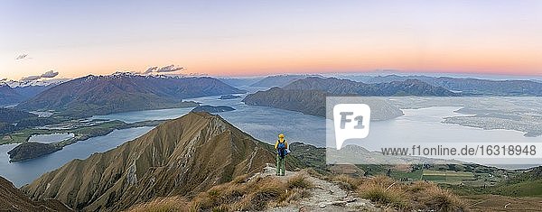 Young man standing on the summit  view of mountains and lake from Mount Roy  Roys Peak at sunset  Lake Wanaka  Southern Alps  Otago  South Island  New Zealand  Oceania
