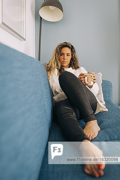 Porträt einer jungen Frau  die sich mit Kaffee auf dem Sofa entspannt