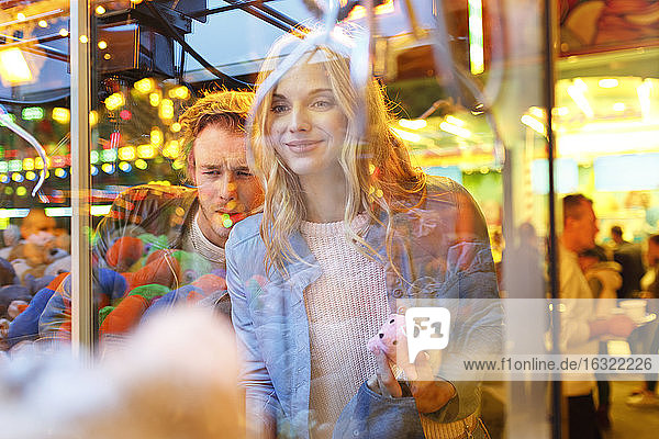 Young couple at fun fair looking at prizes in window