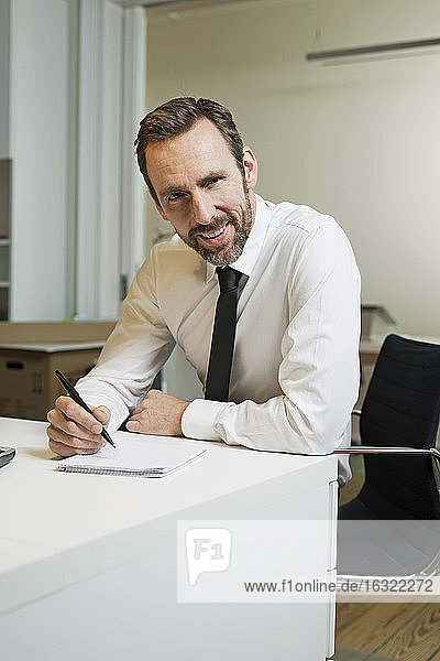 Porträt eines selbstbewussten Geschäftsmannes  der im Büro am Schreibtisch sitzt und Notizen macht
