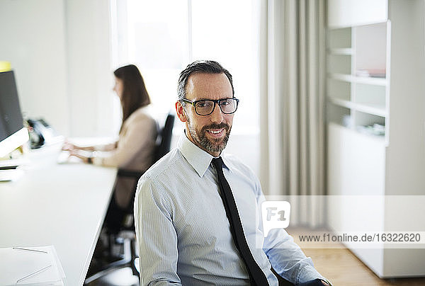 Portrait of confident businessman in office with employee in background