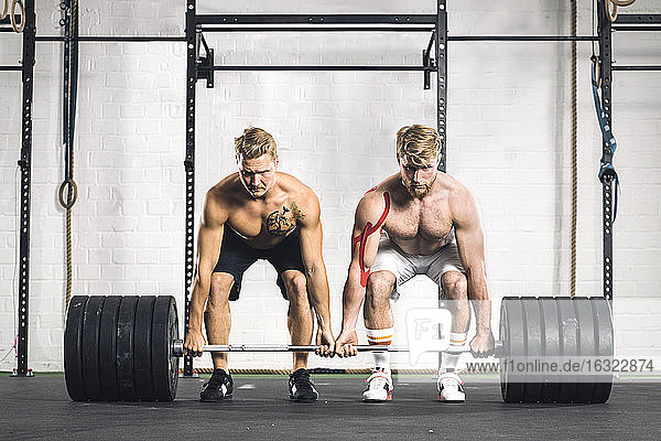 Two young men in gym lifting weights
