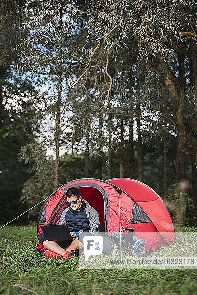 Mann zeltet in Estland  sitzt im Zelt und benutzt einen Laptop