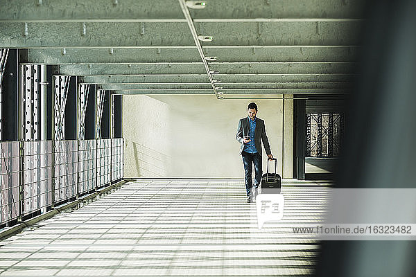 Young businessman walking in car park looking on cell phone