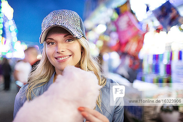 Young woman at fun fair eating candy floss