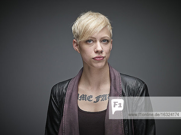 Porträt einer blonden jungen Frau mit Tattoo vor grauem Hintergrund