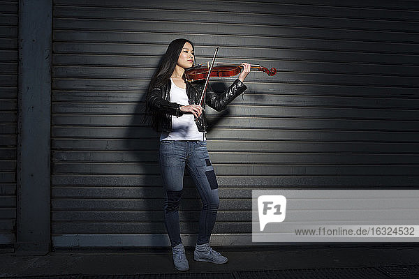 Young female Asian playing violin in front of a roller shutter