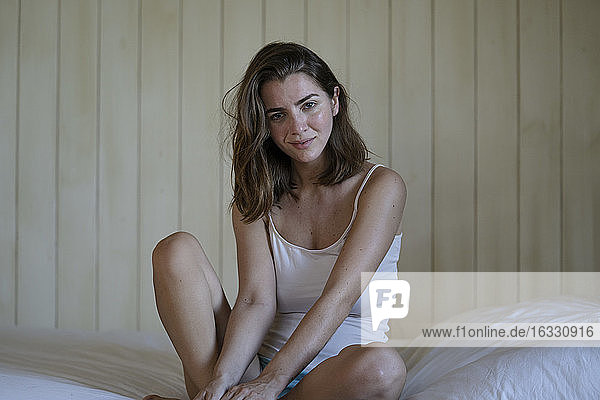 Schöne junge Frau auf dem Bett sitzend