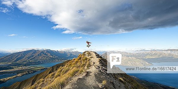 Wanderer macht einen Luftsprung  Ausblick auf Berge und See vom Mount Roy  Roys Peak  Lake Wanaka  Südalpen  Otago  Südinsel  Neuseeland  Ozeanien