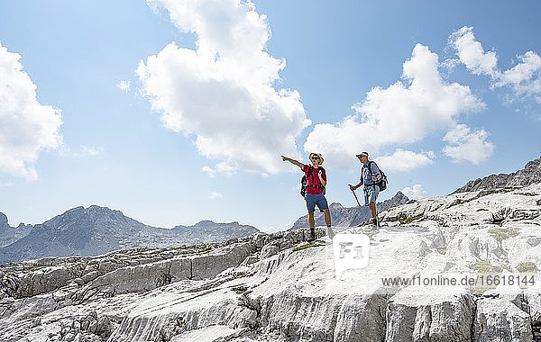 Two hikers on a hiking trail  hiker points into the distance  landscape of washed out karst rocks  Steinernes Meer  Berchtesgaden National Park  Berchtesgadener Land  Upper Bavaria  Bavaria  Germany  Europe