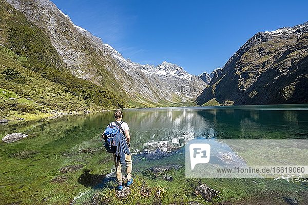 Hiker stands on shore  Lake Marian  Fiordland National Park  Te Anau  Southland  South Island  New Zealand  Oceania