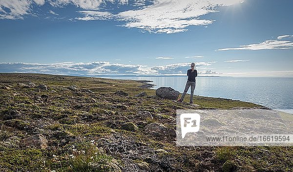 Blonde woman from behind with stands on coast behind sea  Norðurland eystra  Iceland  Europe