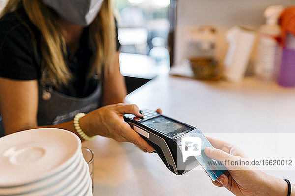 Kassiererin  die von einem Kunden in einem Café während COVID-19 eine Zahlung per Kreditkarte entgegennimmt