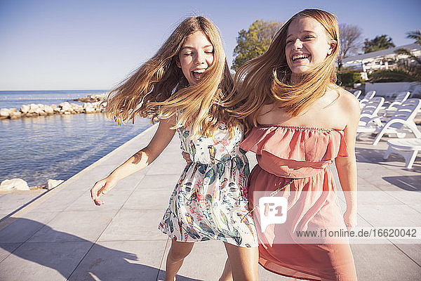 Friends laughing while walking on sidewalk against sea