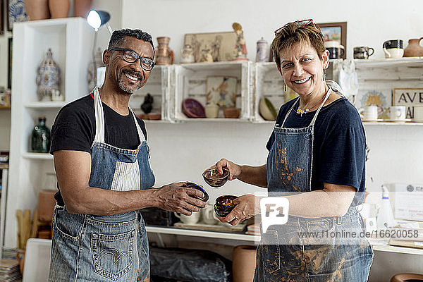 Lächelnde Mitarbeiter  die in der Werkstatt stehen und Keramiken halten