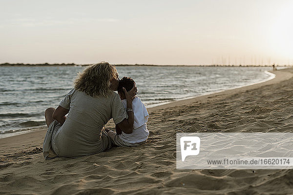 Grandmother kissing grandson while spending leisure time at beach during sunset