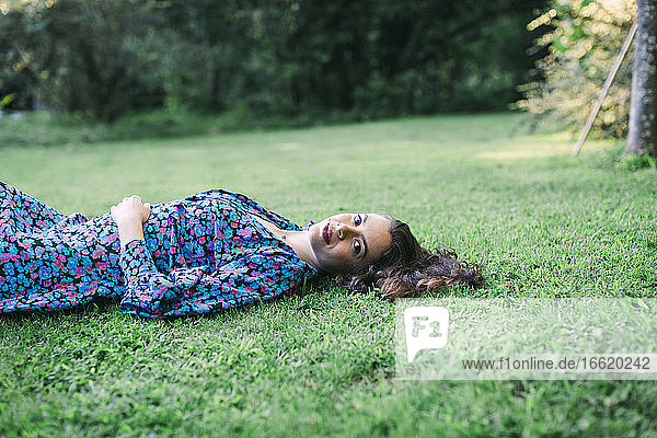 Lächelnde junge Frau auf einer Wiese im Park liegend