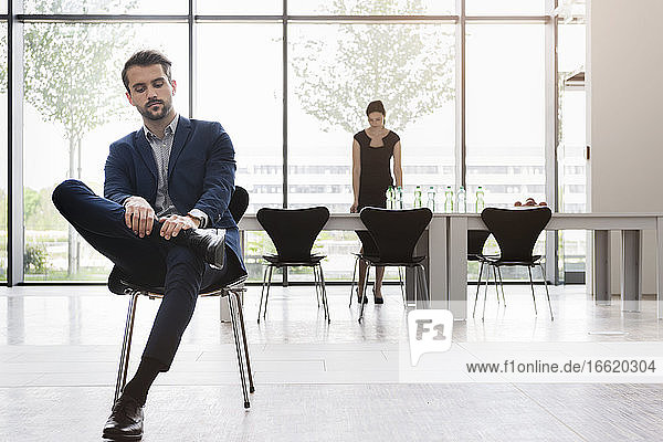 Serious businessman sitting on chair while female coworker working at desk in background