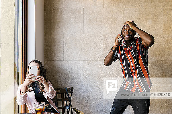 Junger Mann mit Hand auf dem Kopf  während er mit seiner Freundin im Café über sein Smartphone spricht