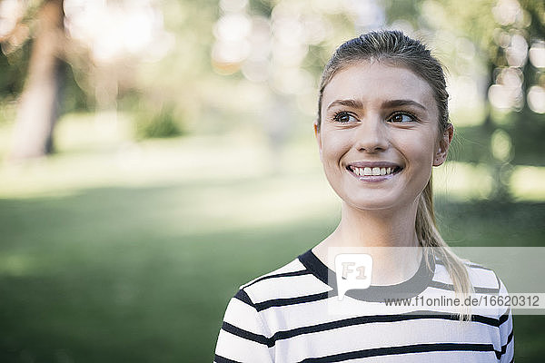 Smiling woman looking away while standing in public park
