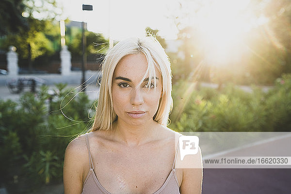 Nahaufnahme einer ernsten jungen Frau mit blondem Haar im Park bei Sonnenuntergang