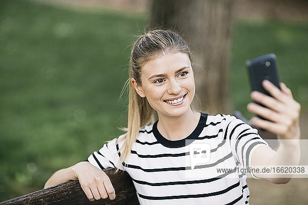 Schöne Frau  die ein Selfie mit ihrem Smartphone macht  während sie in einem öffentlichen Park sitzt