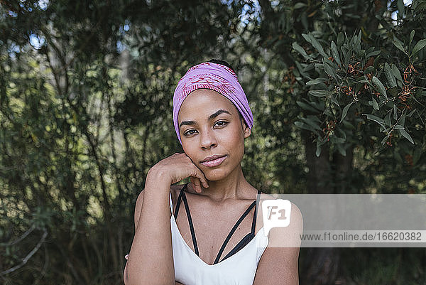 Selbstbewusste junge Frau mit lilafarbenem Kopftuch  die in einem Park vor Pflanzen steht