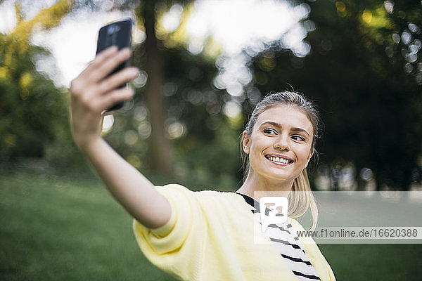 Frau lächelt  während sie ein Selfie in einem öffentlichen Park macht