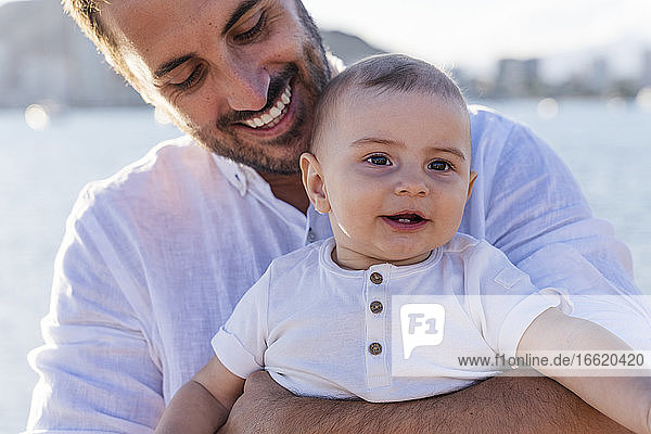 Close-up of smiling father carrying cute son at beach during sunset