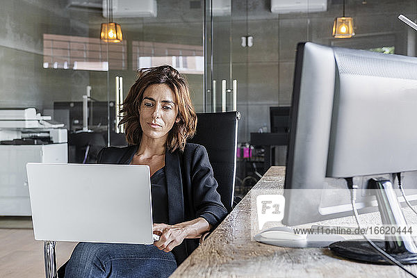 Geschäftsfrau arbeitet am Laptop  während sie auf einem Stuhl im Büro sitzt