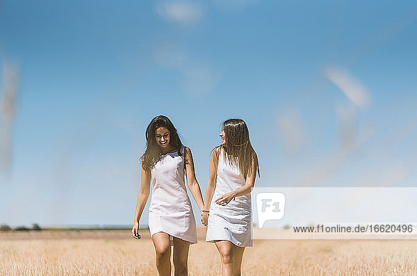 Schönes lesbisches Paar im Gespräch beim Spaziergang auf einem landwirtschaftlichen Feld gegen den klaren Himmel