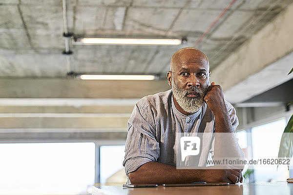 Thoughtful bald man looking away while leaning on table at rooftop