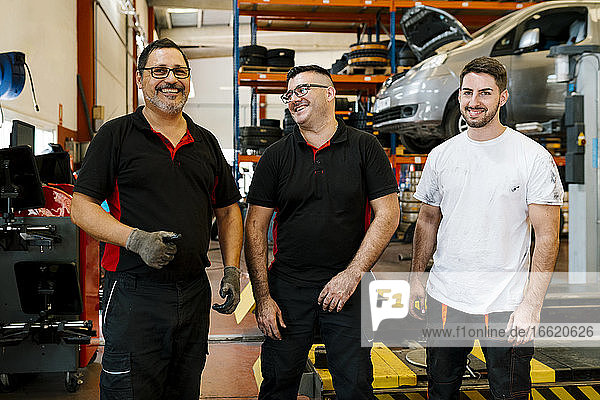 Smiling male coworkers standing in auto repair shop