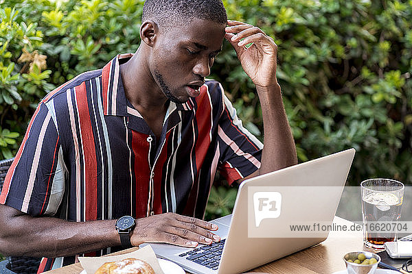 Junger Mann  der einen Laptop benutzt  während er auf der Terrasse eines Cafés sitzt