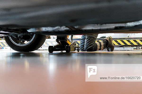 Mechaniker wechselt einen Reifen  während er in einer Autowerkstatt auf dem Boden kniet