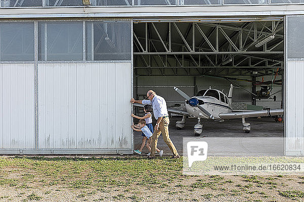 Kinder und Großvater öffnen die Tür eines Flugzeughangars