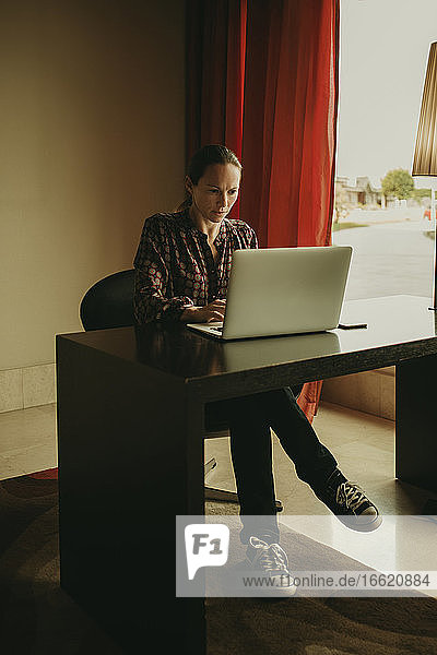 Mittlere erwachsene Frau arbeitet am Laptop  während sie im Büro sitzt